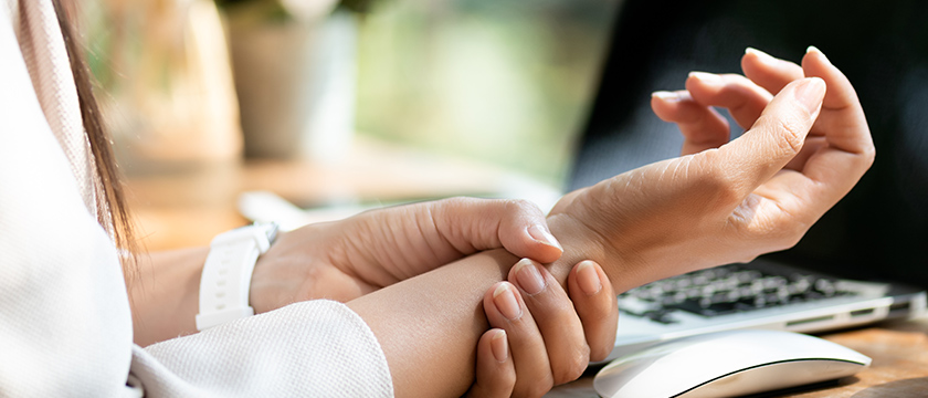 Woman Grasping Her Wrist at Her Computer