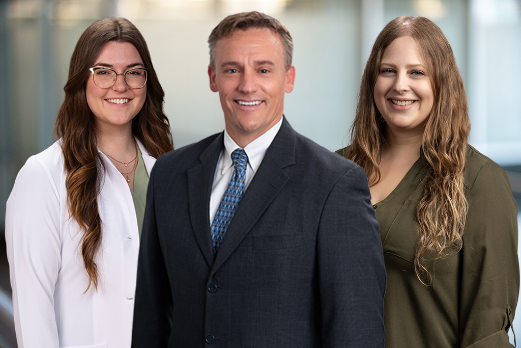 Three orthopedic care team members, including a physician in a suit flanked by two female providers, smiling against a soft-focus background.