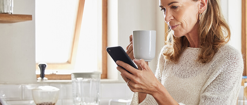 Woman on Cell Phone in Kitchen with Coffee